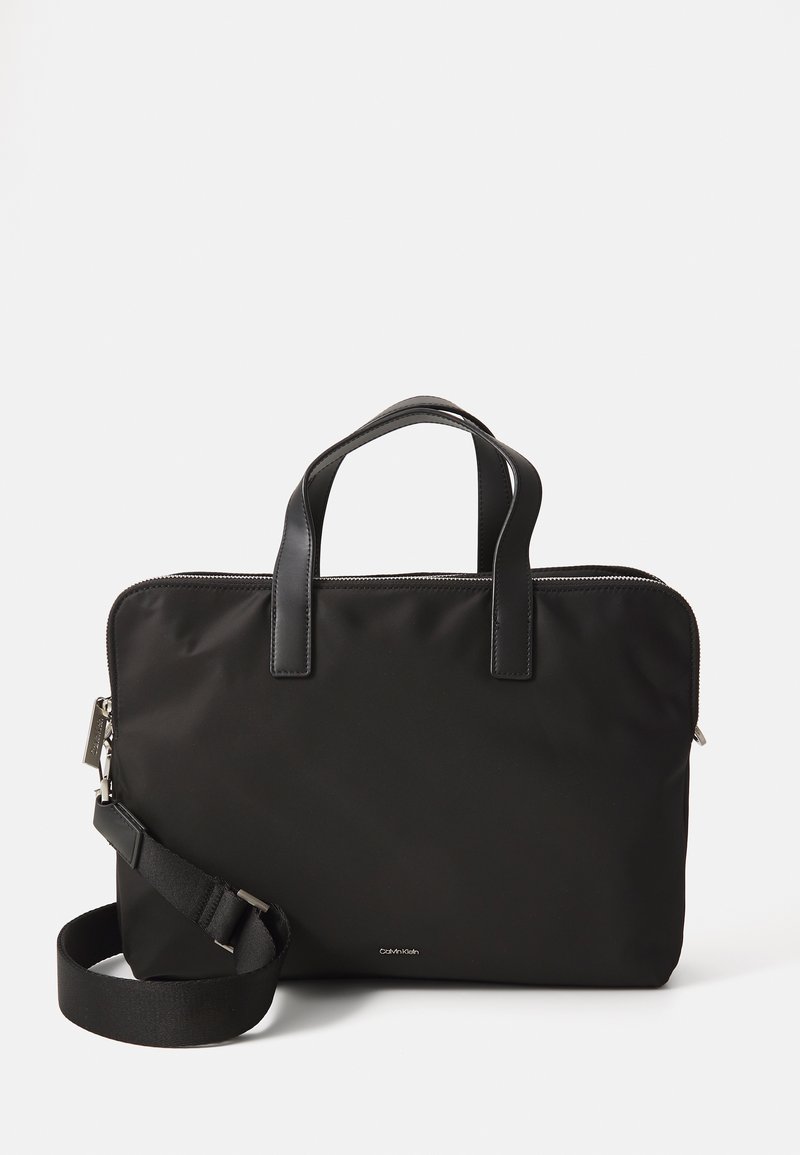 Bolso para portátil negro de nylon con asas de cuero. Cuenta con un cierre de cremallera y una correa desmontable para mayor versatilidad. Diseño minimalista.