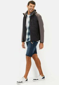 Sort og grå hættejakke med et let design, parret med en ternet skjorte, denimshorts og hvide sneakers.