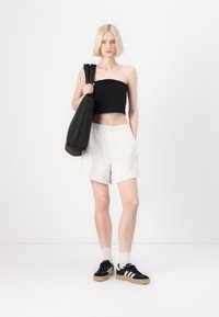 Svart strapless topp, ljusgrå shorts och svarta sneakers med vita ränder. Svart tote-väska, släta texturer och avslappnad passform.