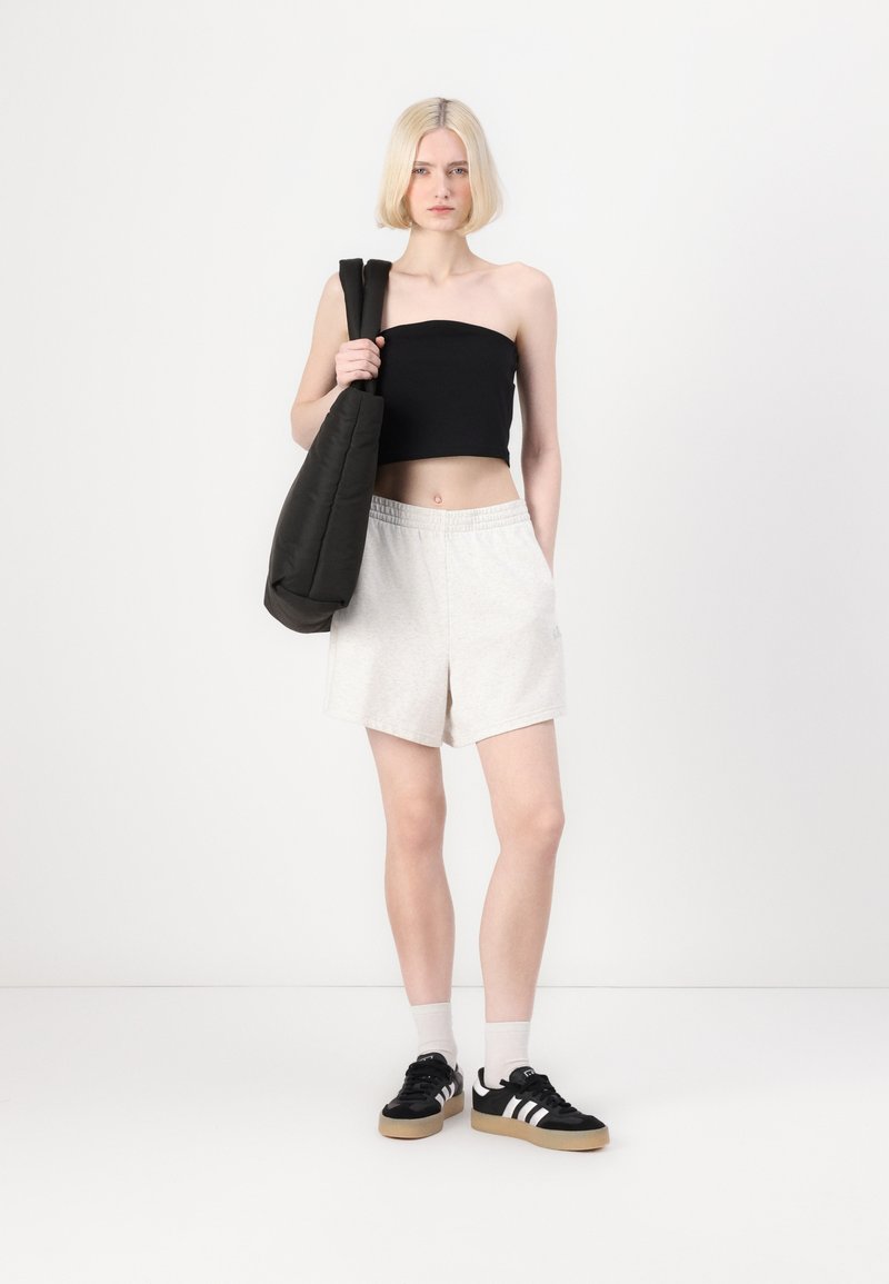 Svart strapless topp, ljusgrå shorts och svarta sneakers med vita ränder. Svart tote-väska, släta texturer och avslappnad passform.