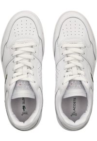 Weiße Leder-Sneaker mit perforierten Details, flachen Schnürsenkeln und einem markierten Fußbett. Auf der Seite befindet sich ein grünes Krokodil-Logo.