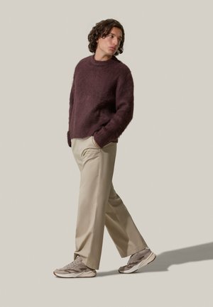 Pull maroon oversize in maglia con finitura texturizzata, abbinato a pantaloni beige chiaro e sneakers grigie con accenti più scuri.