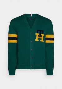 Grøn cardigan med V-halsdesign, der har gule og navy-stribede ærmer. Foran lommer og et logo-mærke. Blødt, tekstureret stof.