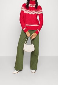 Red knit sweater with white zigzag pattern, paired with olive green wide-leg pants and a small white handbag. Model wearing white ankle boots.