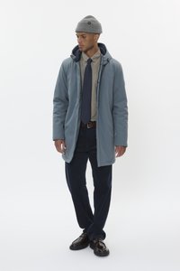 Svetlo modri vodoodporni plašč s kapuco, bež srajca s ovratnikom, mornarsko modra kravata, mornarsko modri kordni hlače in temno rjavi čevlji. Sivi pleteni klobuk na glavi.