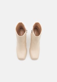 Paire de bottines beiges à bouts carrés avec fermetures éclair latérales, vues de dessus sur un fond blanc uni.
