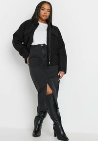 Svart, texturerad fluffig jacka med dragkedja och fickor med klaff, i kombination med en svart denimkjol med en hög slits och knähöga svarta stövlar.