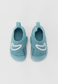 Sininen tekstiilistä valmistettu liukupohjainen kenkä, jossa on teksturoitu pinta, valkoinen Nike-logo ja takana vetokohdat helppoa pukemista varten.