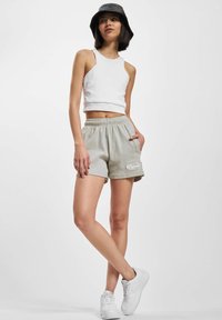 Gaiši pelēki riboti šorti ar elastīgu jostasvietu, kas aprīkoti ar sānu kabatām un baltu izšūtu logotipu. Saskaņoti ar baltu kroptu topu un baltām sporta kurpēm.