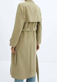 Cappotto trench beige con vita cintrata, dettaglio in capa sul retro e maniche lunghe. Progettato con una texture liscia e uno stile minimalista.