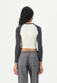 Raglan sleeve, cropped top in cream and navy, fitted design; paired with grey cargo pants featuring front and back pockets.