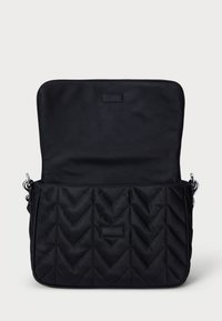 Črna prešita torba preko ramena s chevron vzorcem, ki ima gladko notranjost in srebrno strojno opremo. Odprta preklopna zapirala razkrije prostoren predel.