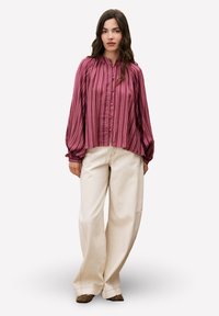 Chemise à boutons de couleur rose profond avec des rayures verticales, dotée de manches longues et d'un col froncé. Associée à un pantalon large crème.