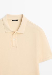 Polo beige à manches courtes avec deux boutons blancs et un col, présenté à plat sur fond blanc.
