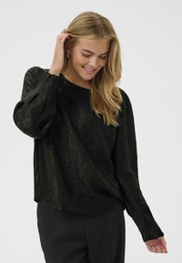Schwarze strukturierte Bluse mit langen Ärmeln, rundem Ausschnitt und dezenten Falten. Der Stoff wirkt leicht und hat einen sanften Glanz.