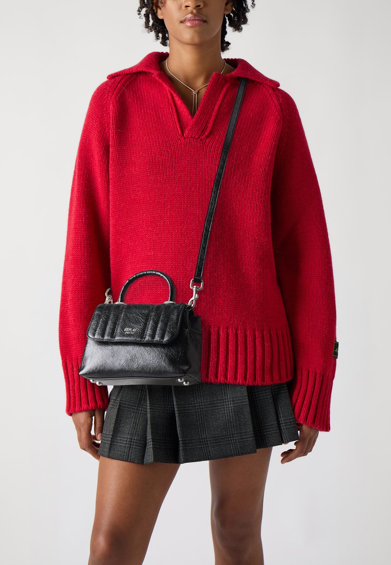 Pull en tricot rouge avec un décolleté en V profond et un ourlet côtelé. Sac à main matelassé noir avec une poignée supérieure et une bandoulière amovible. Jupe en tartan.