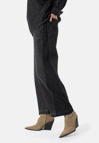 Svarte vide jeans med sidesømmer og frynsete kanter, kombinert med beige spisse ankelstøvler med teksturert overdel og kilehæl.