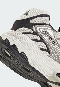 Szaro-czarny but sportowy z teksturowaną siateczkową cholewką, odblaskowymi elementami oraz wzorzystą gumową podeszwą zapewniającą przyczepność. Widoczny sześciokątny detal.