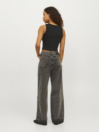 Svart ribbad crop-top i kombination med mörkgrå vida jeans med hög midja och uppvikta fållar, med bakfickor synliga.