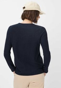 Marineblaue, gerippte Langarmbluse mit Rundhalsausschnitt, strukturiertem Stoff und lockerer Passform. Kombiniert mit einer beigen Cap, die einen lässigen Stil zeigt.