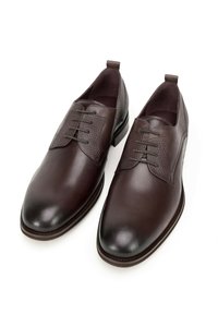 Zapatos de vestir de cuero marrón con un acabado suave, paneles laterales texturizados, seis ojetes y un tacón bajo. Cuenta con lengüetas para facilitar su uso.