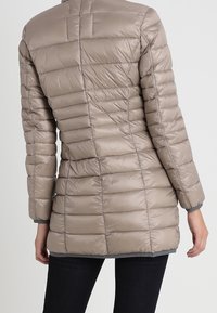 Padded jacket v světle béžové barvě, s horizontálním prošívaným designem, dlouhými rukávy, vysokým límcem a šedými akcenty na manžetách a dolním lemu.