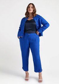 Giacca di lino blu e pantaloni abbinati, vestibilità rilassata, con chiusura a bottone e risvolti. Abbinata a un canottiera di satin blu notte.
