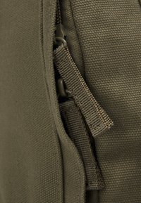 Sac en tissu vert olive avec surface texturée. Équipé d'une fermeture éclair et d'une languette en sangle, mettant en valeur des coutures durables et des bords nets.