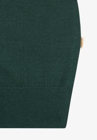 Σκούρο πράσινο πλεκτό ύφασμα με ραμμένη άκρη και μια μικρή μπεζ ετικέτα με πορτοκαλί κείμενο στο πλάι.