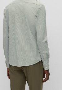 Lang shirt met een groen-wit micropatroon, manchetten met knopen en een afgeronde zoom. De stof oogt lichtgewicht met een gladde textuur.