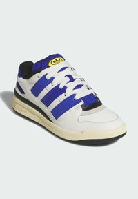 White sneaker with purple stripes, black accents, and mesh details. Features white laces, a textured sole, and a yellow logo on the tongue.