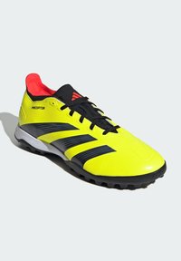 Botte de football jaune vif avec des accents noirs, en matériau synthétique texturé, design à lacets, et doublure intérieure rouge. Présente un logo proéminent.