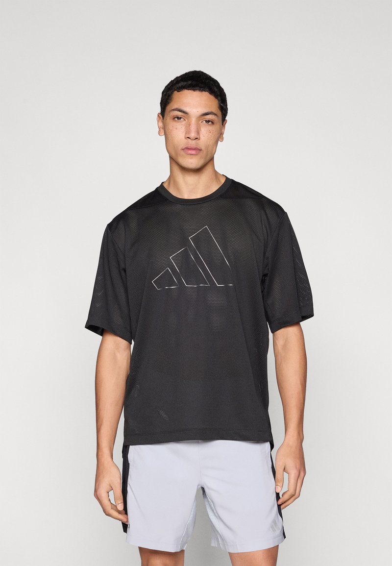 Μαύρο αθλητικό μπλουζάκι με κοντά μανίκια από δίχτυ, με εμφανές ασημένιο λογότυπο Adidas στο μπροστινό μέρος. Φοριέται με ανοιχτό γκρι σορτς.