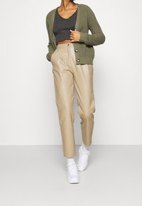 Oliwkowo zielony dziergany kardigan, szary krótki top, beżowe spodnie ze sztucznej skóry oraz białe trampki. Charakterystyczne są guziki i gładkie tekstury.