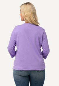 Blusa de manga larga en color lavanda, hecha de una tela suave, con un cuello redondo y un corte relajado, combinada con vaqueros de tiro medio en azul oscuro.