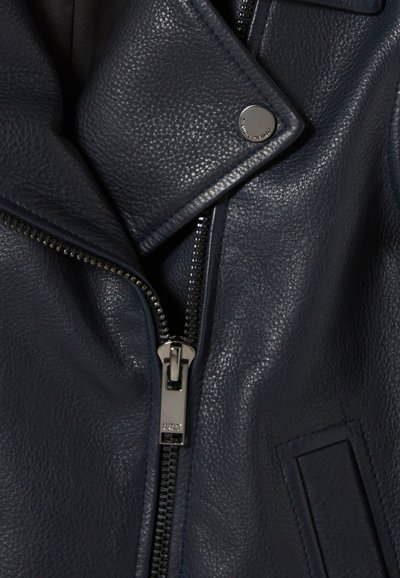 Veste en cuir bleu marine avec fermeture éclair, coutures contrastées et détail à bouton-pression sur le col. Fini texturé.