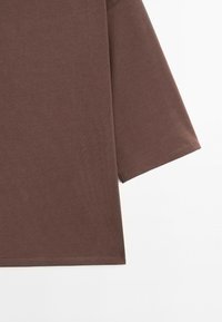 Close-up of brown fabric with a straight hem and a three-quarter sleeve on a white background.