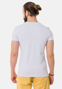 Weisses Kurzarm-T-Shirt mit rundem Ausschnitt, glatter Textur und taillierter Passform, getragen mit gelben Hosen.