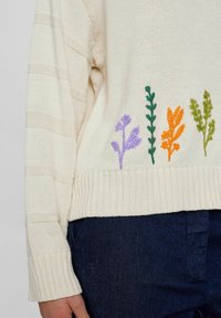 Maglione a maglia color crema con strisce orizzontali e disegni floreali ricamati in viola, verde, arancione e verde scuro all'orlo.