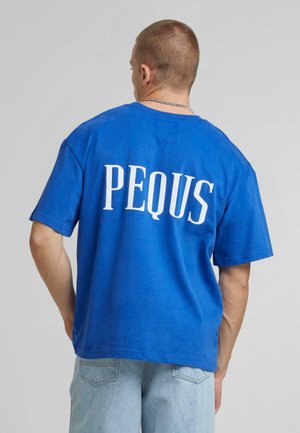 Camiseta azul de algodón con mangas cortas y ajuste holgado, con la palabra "PEQUS" en grandes letras blancas en la parte trasera.