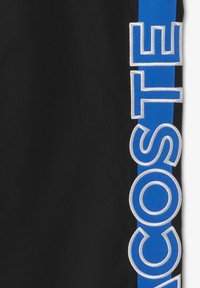 Zwarte shorts met een blauwe zijstreep en witte geborduurde "LACOSTE" tekst. Lichtgewicht stof met een gladde textuur.