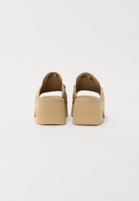 Beige platform sandalen met een open achterkant, zachte suède textuur en vierkante blokhak. Minimalistisch ontwerp zonder zichtbare hardware.