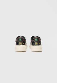 Černé tenisky s tlustými bílými podrážkami, zdobené barevnými geometrickými a logovými vzory v oblasti paty, z pohledu zezadu.