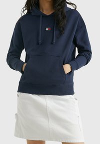 Felpa con cappuccio blu navy, in misto cotone, presenta una tasca frontale, dettagli con cordino e una piccola patch con logo sul petto.