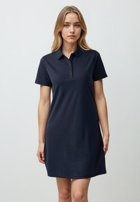 Donkerblauwe polojurk gemaakt van een zachte katoenmengeling, met een kraaghalslijn, korte mouwen en een vierknops sluiting.