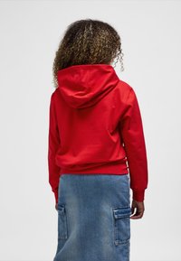 Rotes Kapuzen-Sweatshirt mit lockerem Schnitt, gerippten Bündchen und Saum, kombiniert mit einem blauen Jeansrock mit großen Seitentaschen.