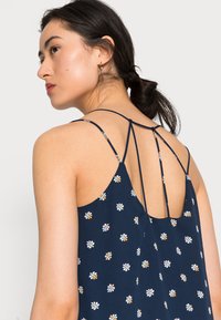 Vestido floral azul marinho com costas baixas, apresentando alças finas e um design em camadas. Pequenos padrões de flores coloridas estão espalhados por todo o vestido.
