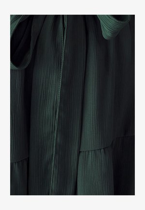 Garšs, tumši zaļš kleita ar teksturētu, krokotu audumu. Tam ir aukliņas detaļa jostas vietā, ar gludu virsmu un vertikālām šuvēm.