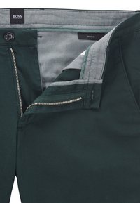 Ciemnozielone spodnie z szarą podszewką, wyposażone w suwak i zapięcie na guzik. Wykonane z elastycznego materiału o eleganckim kroju z minimalną liczbą elementów metalowych.