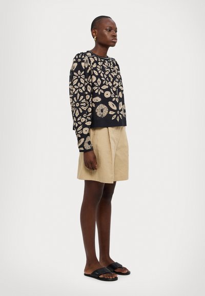 Pull noir avec des motifs floraux beiges, col rond et manches longues, assorti à un short beige et des sandales noires à enfiler.